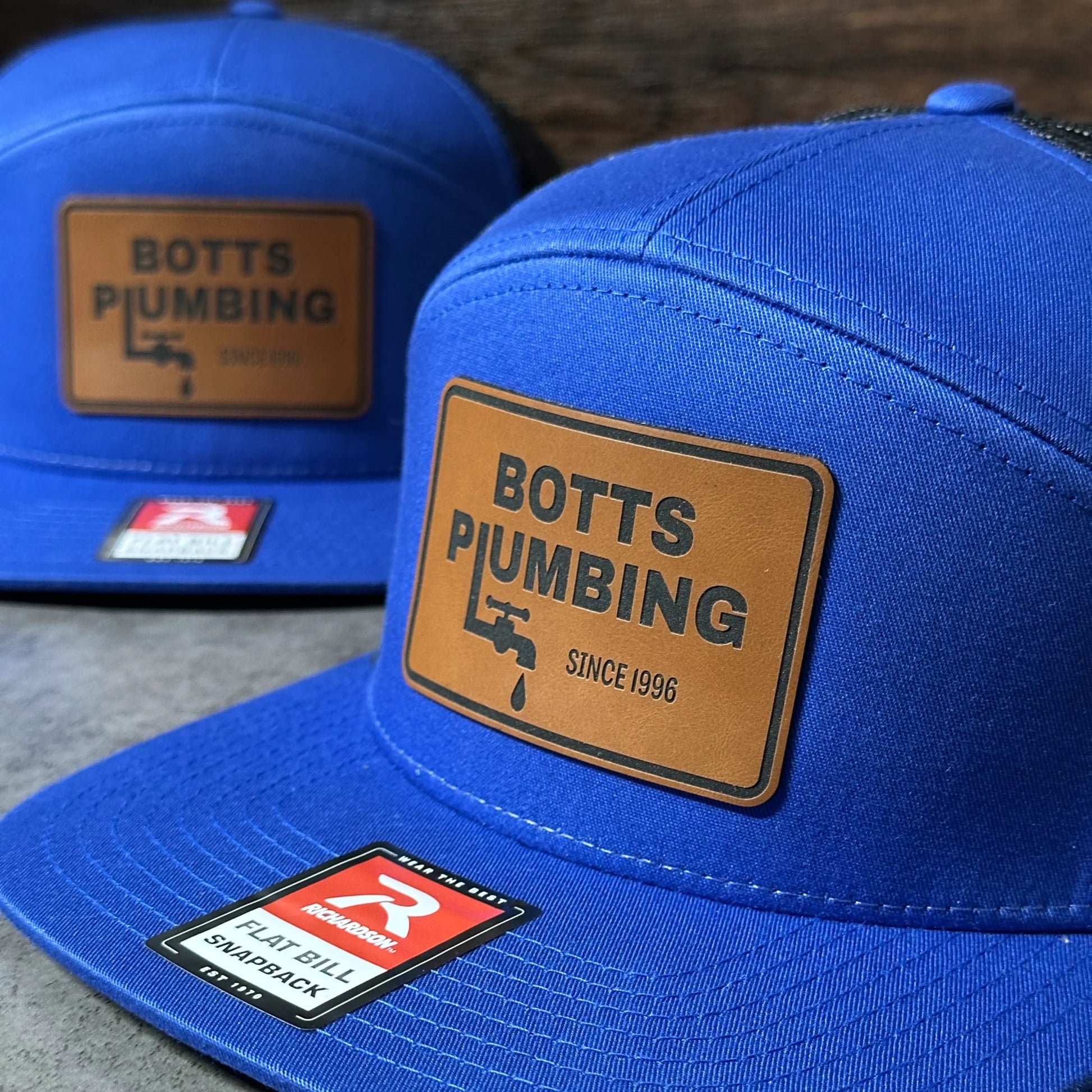 a pair of blue baseball caps with various logos and text on them.