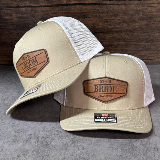 two beige baseball caps with a logo on them, placed on a wooden surface.