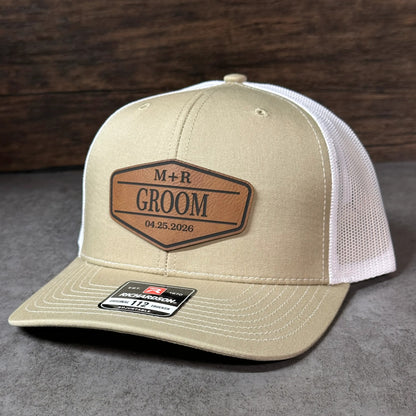 A beige baseball cap with a mesh panel and a leather patch on the front, displaying a personalized message.