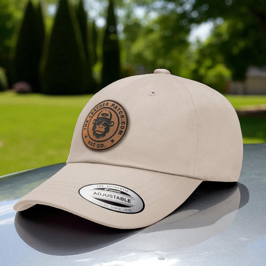 A beige baseball cap with a circular patch featuring a cartoon character and text, placed on a car hood.