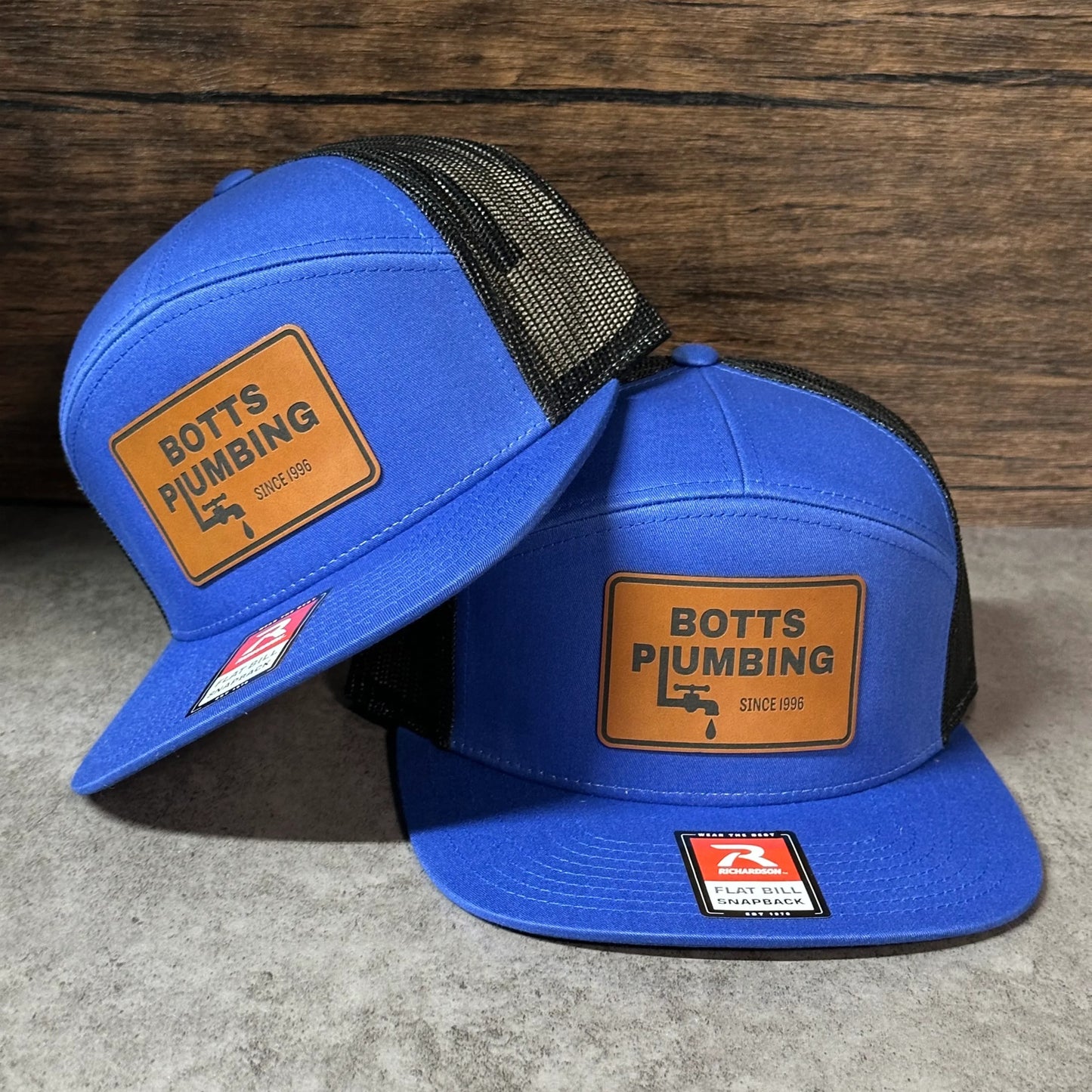 two blue baseball caps with the text "BOTTS PUMBING" printed on them.