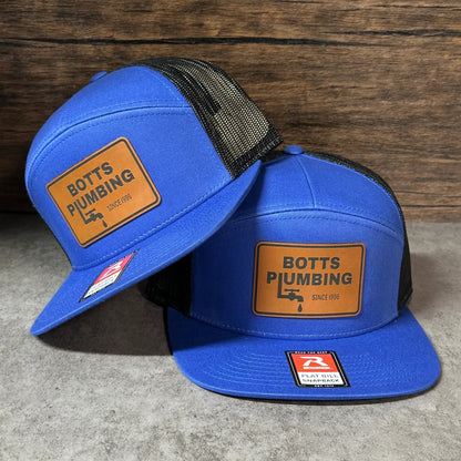 two blue baseball caps with the text "BOTTS PUMBING" printed on them.